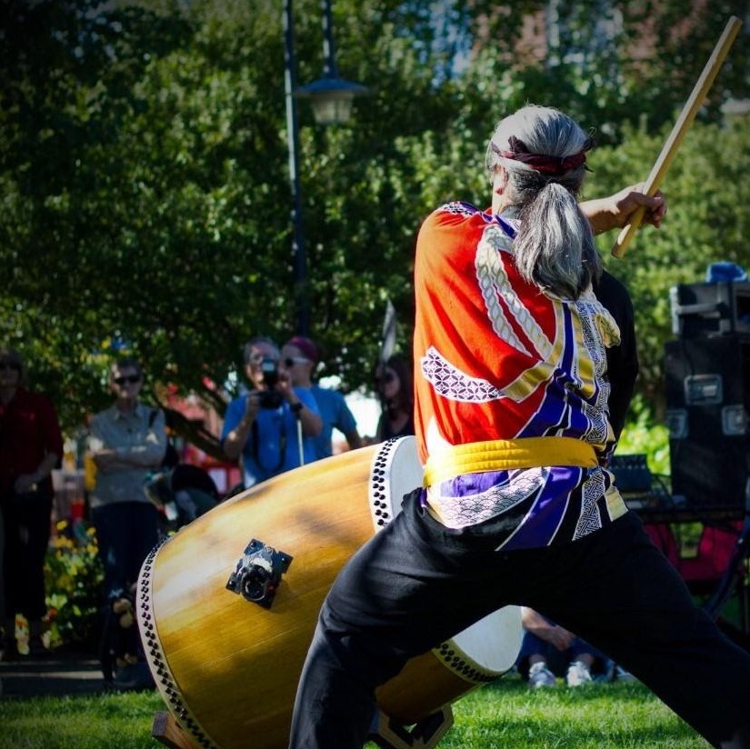 Taiko performer posed to strike a drum outside on a lawn